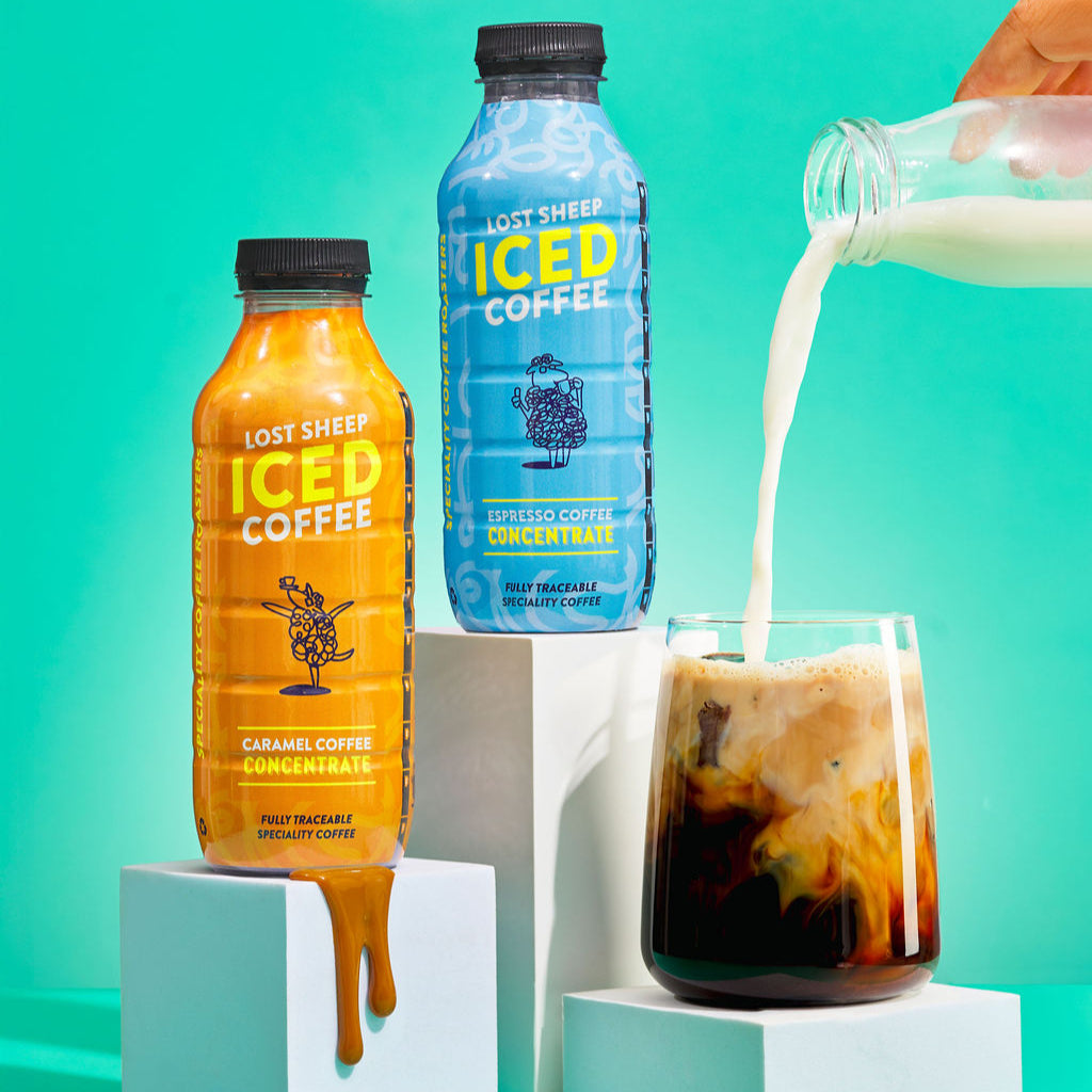 Lost Sheep iced coffee concentrate bottles with a glass of iced coffee and milk being poured against a teal background.