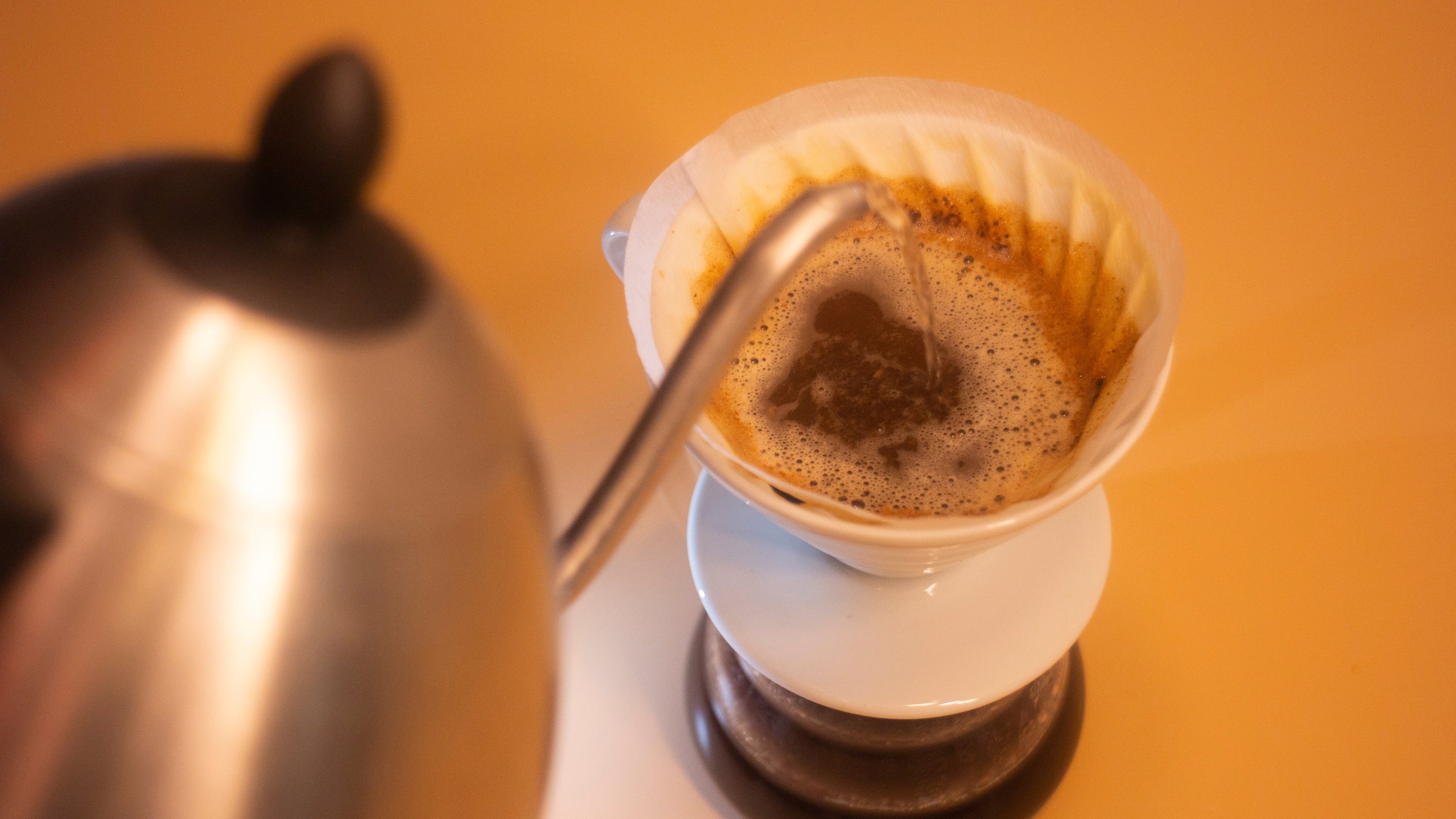 Coffee being poured into a filter with a kettle on a yellow background