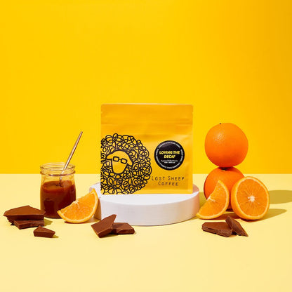 Lost Sheep Coffee's Decaf in yellow packaging surrounded by Milk chocolate, orange and caramel tasting notes