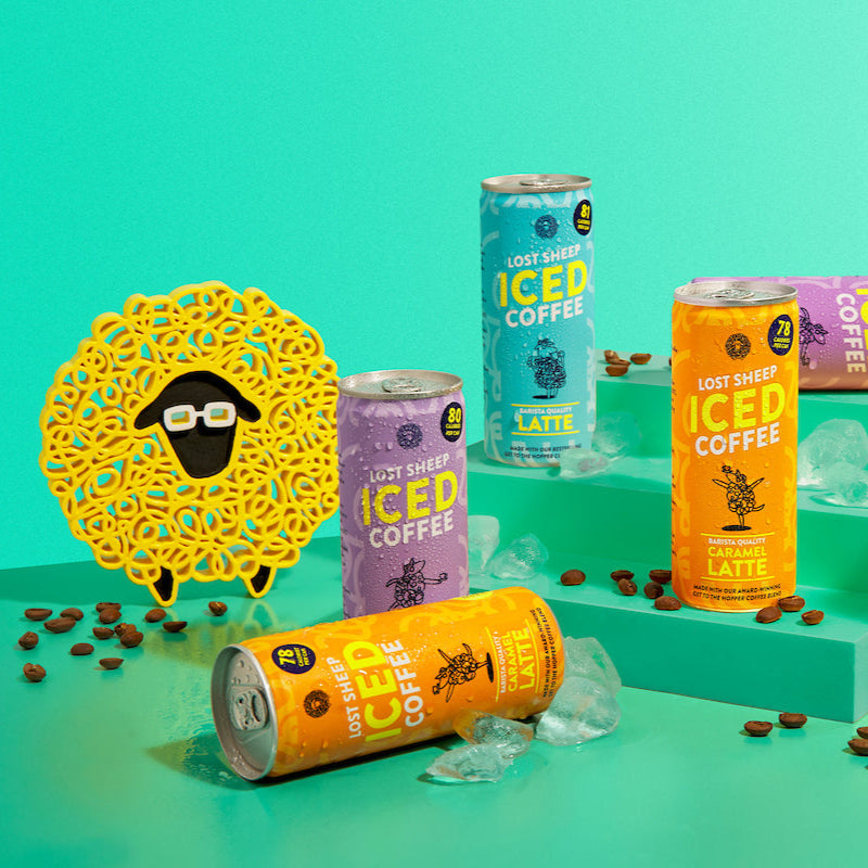 A collection of Ready To Drink Iced Coffee cans in various flavors, with decorative elements and coffee beans scattered around.